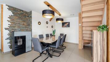 A modern dining area with a wooden table, grey chairs, a black-framed fireplace, and a stone wall.