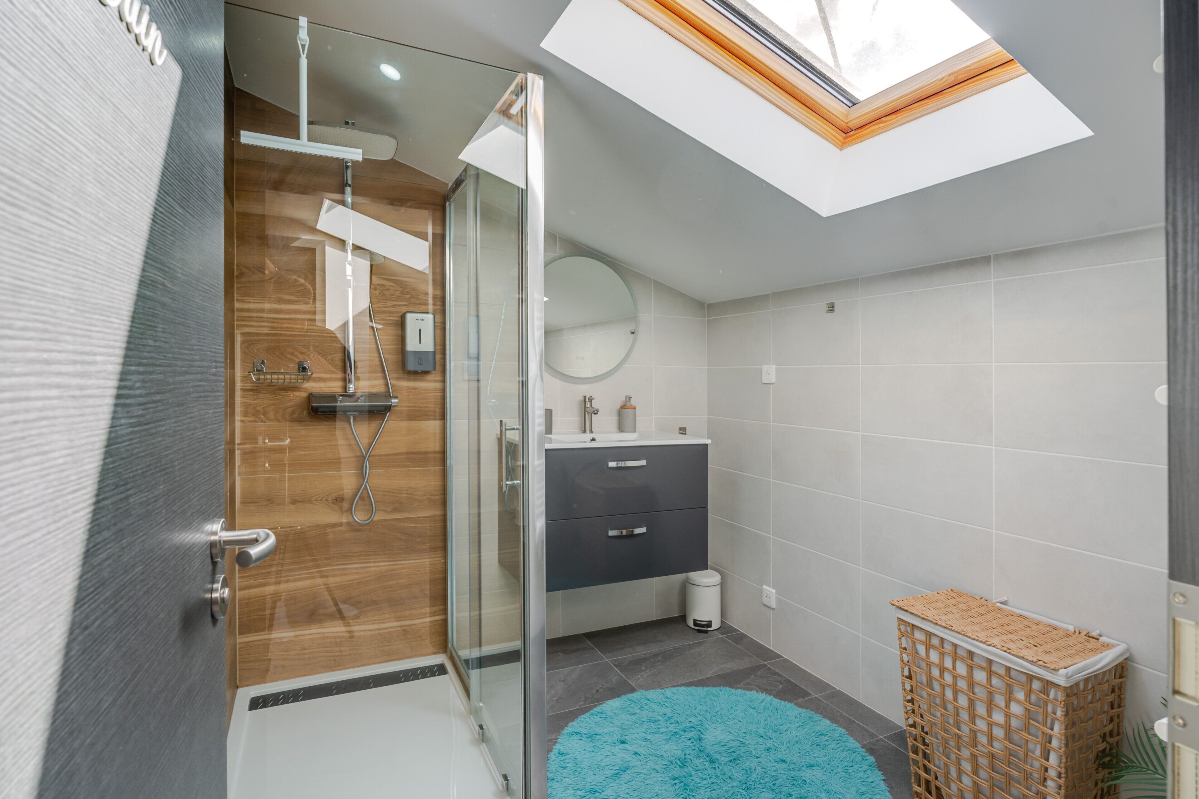 A modern bathroom with a skylight, a glass shower enclosure, a sink, and a round mirror.