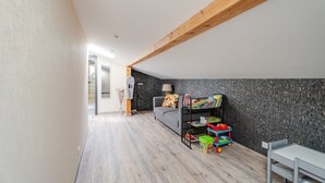 Un interior moderno con techo de vigas de madera, un sofá gris, una estantería con juguetes infantiles y una pequeña mesa.