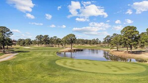 Um campo de golfe com lago, árvores e céu claro.