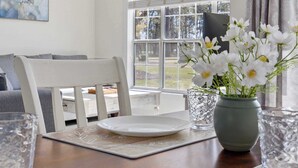 Uma mesa de jantar com um prato branco, um vaso com flores brancas e um copo.