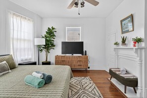 Ein Schlafzimmer mit Bett, Fernseher, Pflanze, Kamin und Fenster.
