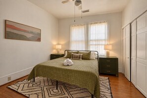 A bedroom with a bed, two bedside tables with lamps, a window with curtains, a painting on the wall, and a wardrobe. - Front Street Historic Loft | Close to Dining, Bars & Riverwalk (Wilmington)