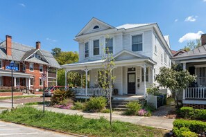 A two-story white house with a front porch, a garage, and a brick building across the street. - Front Street Historic Loft | Close to Dining, Bars & Riverwalk (Wilmington)