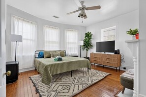 A bedroom with a bed, a TV, a dresser, a plant, and a ceiling fan. - Front Street Historic Loft | Close to Dining, Bars & Riverwalk (Wilmington)