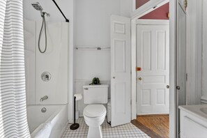 A bathroom with a shower, toilet, and a door leading to another room. - Front Street Historic Loft | Close to Dining, Bars & Riverwalk (Wilmington)