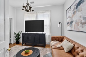 Ein Wohnzimmer mit Fernseher, Sofa, Couchtisch und einer Pflanze.