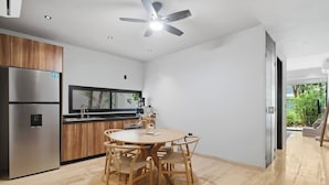 Une cuisine moderne dotée d’un réfrigérateur encastré, de meubles de rangement en bois, d’une table de salle à manger ronde avec des chaises et d’un ventilateur de plafond.