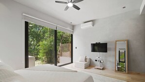 Une chambre à coucher comprenant un lit, une télévision, un miroir et une porte-fenêtre coulissante donnant sur un balcon.