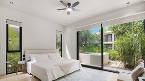 Une chambre avec un lit, un ventilateur de plafond, une grande fenêtre et une vue sur la verdure.