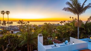 A rooftop with a view of the sunset over the ocean, surrounded by palm trees and houses. - Sunsets at the Shore House (San Diego)