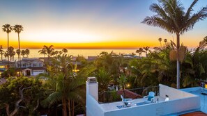 Eine Dachterrasse mit Blick auf den Sonnenuntergang über dem Meer, umgeben von Palmen und Häusern.