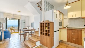 A modern kitchen with wooden cabinets, a built-in oven, and a dining area with a table and chairs. - MALLORCA 13 Canyelles Roses (Rosas / Roses)