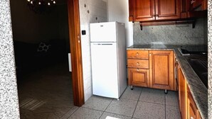 Een keuken met houten kastjes, een witte koelkast en een hangende lamp.