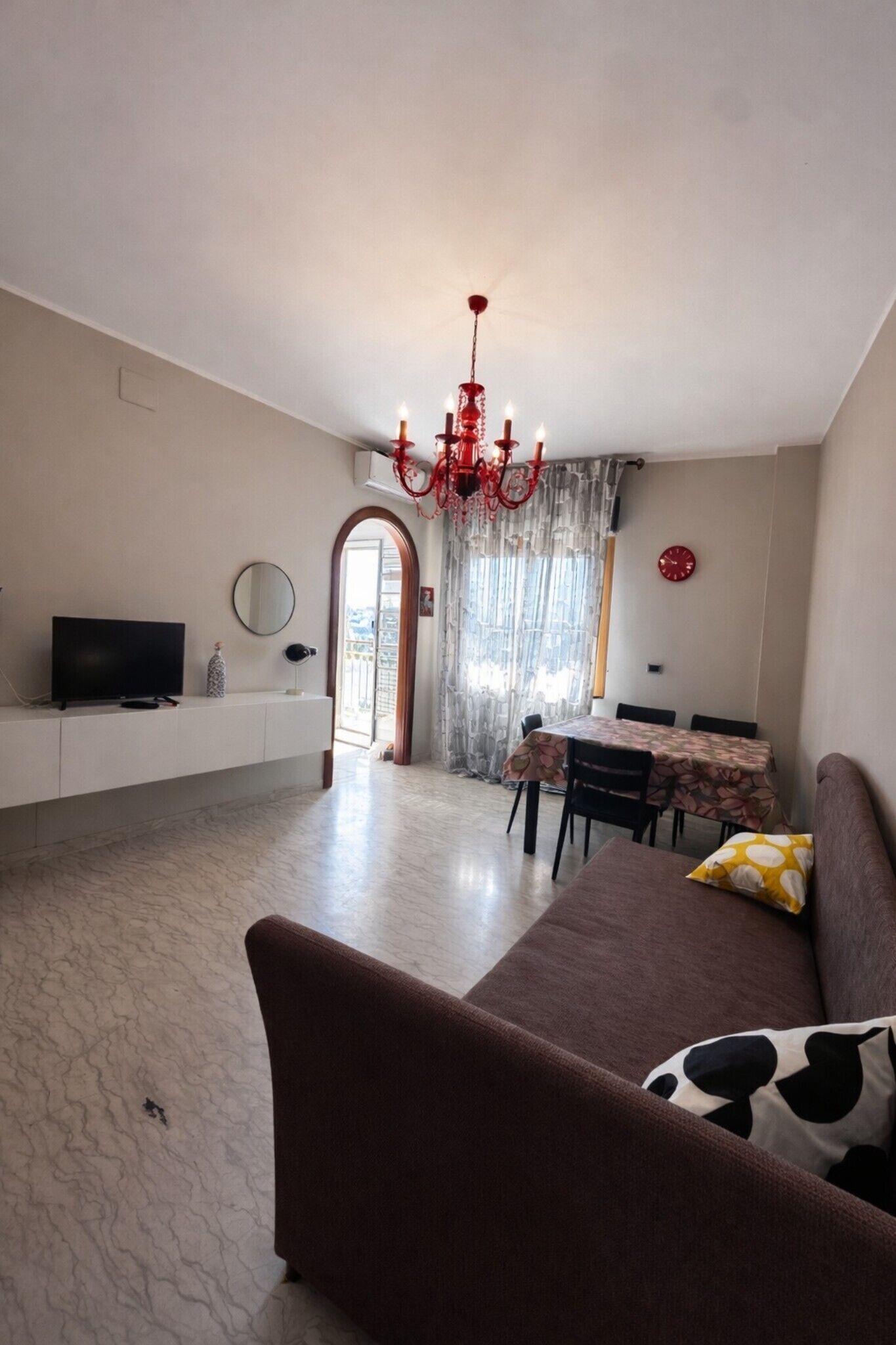 Un salon comprenant un canapé, un téléviseur, un lustre et un coin repas avec une table et des chaises.