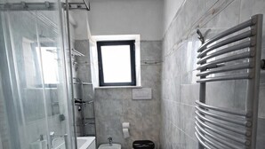 Een badkamer met een douchecabine van glas, een raam, een toilet en een radiator.