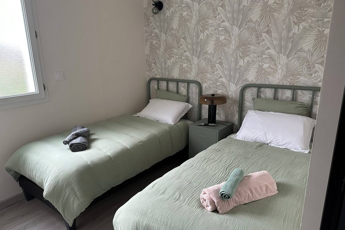A twin room with two beds, a nightstand with a lamp, and a window.