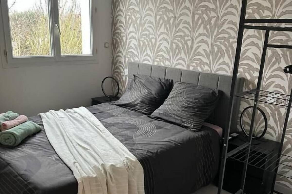 A bedroom with a bed, a bedside table, a wall-mounted lamp, and a window.