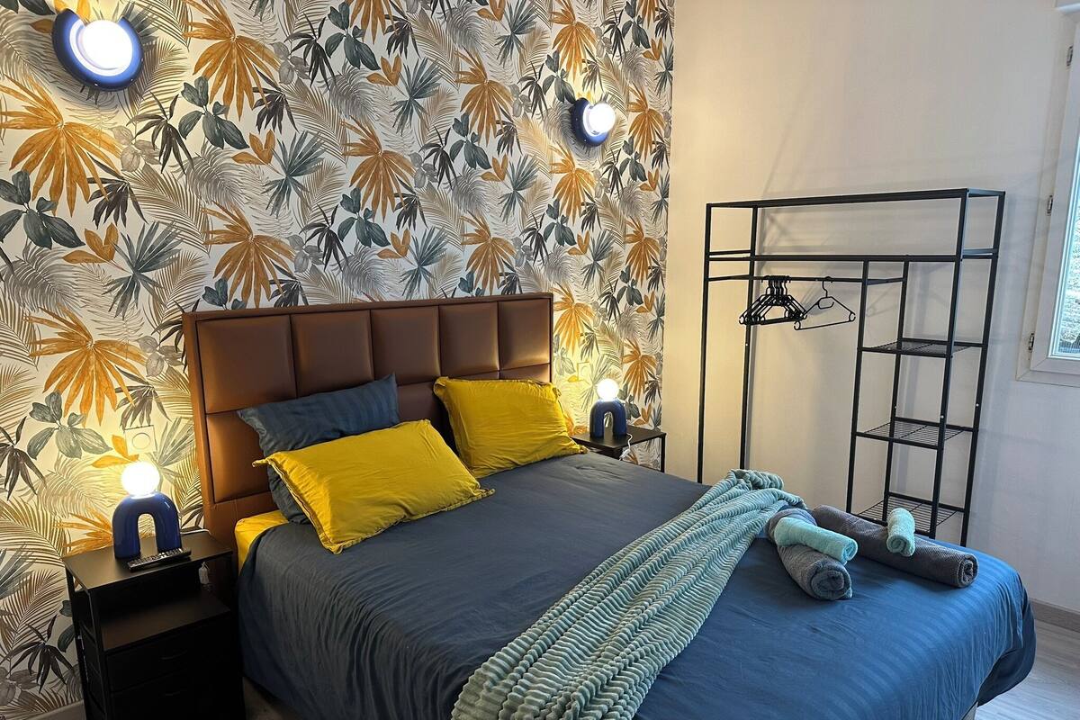 A bedroom with a bed, nightstands, a wall-mounted shelf, and a patterned wallpaper.