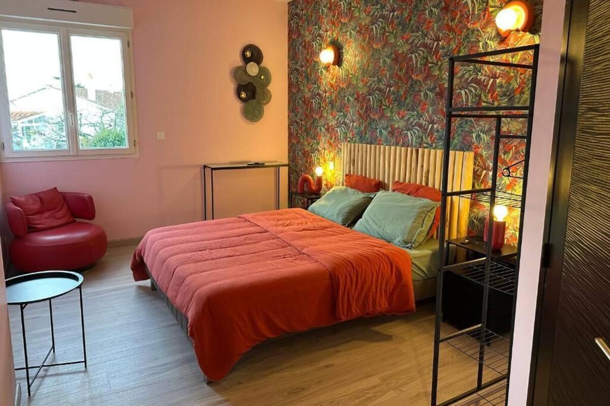 A bedroom with a bed, a red chair, a small table, a radiator, and a window.