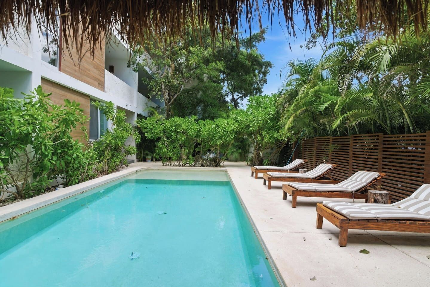 Ein Pool mit Liegestühlen, umgeben von Grünflächen und einem modernen Gebäude.