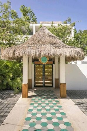 A building with a thatched roof entrance, a tiled walkway, and a sign with a circular emblem. - Unwind in Tulum | Pool & Private Patio (Tulum)