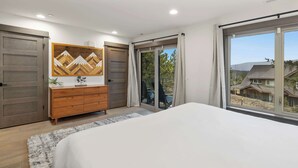Un dormitorio con una cama grande, un aparador de madera y un ventanal corredera que da a un balcón.
