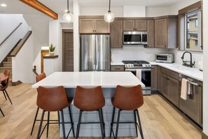 A modern kitchen with stainless steel appliances, a central island with bar stools, and a staircase leading to an upper level. - 3BR Chef Kitch GameRM BBQ Steps to Hike Bike Golf Spa (Cle Elum)