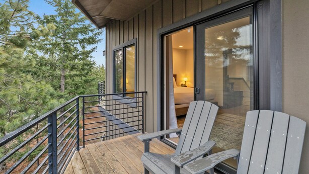 Una terraza de madera con sillas Adirondack, una puerta de cristal que da a un dormitorio y vistas a árboles.