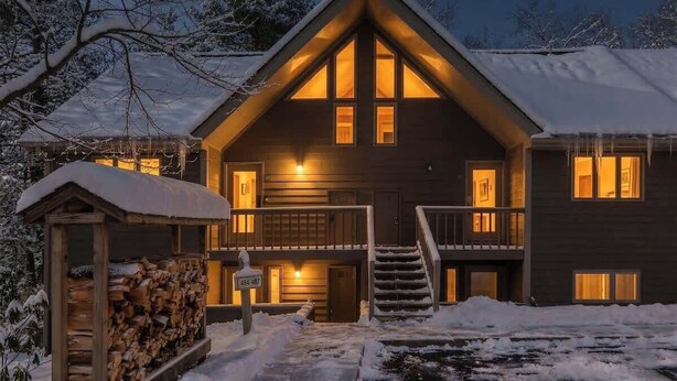 Une cabane en rondins à deux étages, dotée d’un balcon, d’un escalier et d’un toit recouvert de neige.