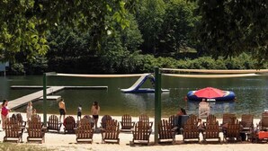 Un parc au bord du lac, avec des chaises en bois, un toboggan aquatique et un radeau gonflable rouge.