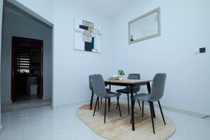 Un comedor con una mesa redonda, cuatro sillas, un tapete, un espejo en la pared y una obra de arte abstracta.