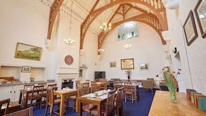 A spacious dining area with wooden tables and chairs, a fireplace, and a large window.