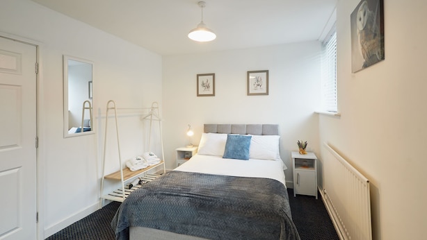 A hotel room with a bed, bedside tables, a radiator, a mirror, and framed pictures on the wall.