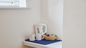 A white shelf with a white coffee maker, two white mugs, and a basket with items.