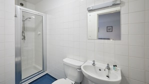 A bathroom with a glass-enclosed shower, a toilet, and a sink with a mirror above it.