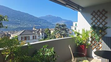 Un balcon donnant sur la ville et les montagnes, avec une chaise et une table.
