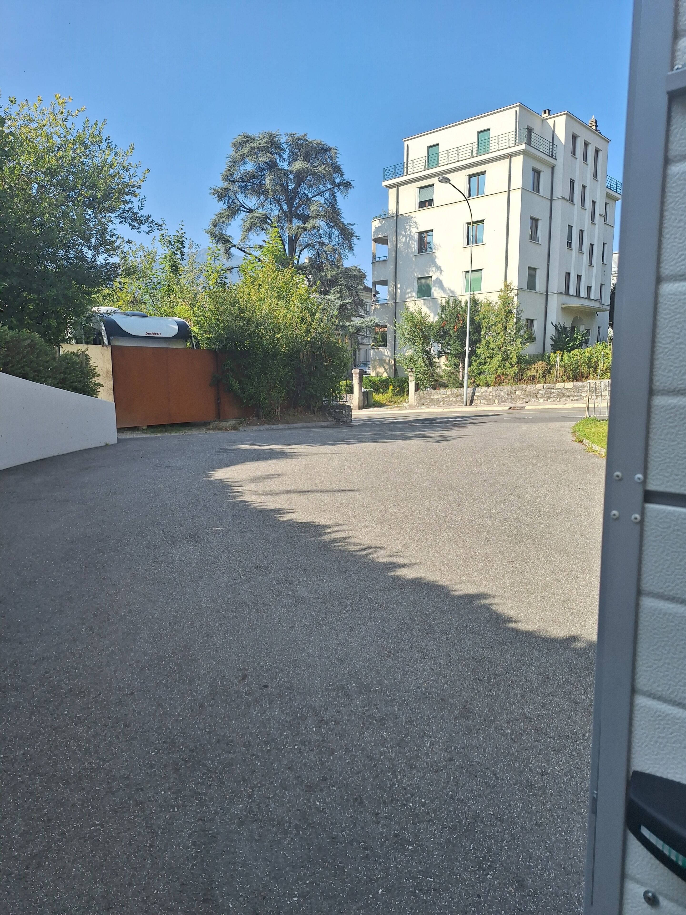 Un quartier résidentiel avec une route asphaltée, un immeuble blanc doté de balcons et de nombreux espaces verts.