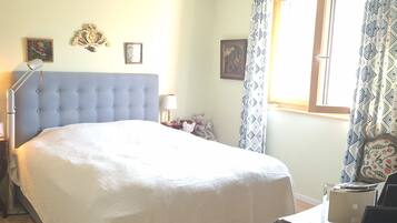 Une chambre à coucher avec un grand lit, une table de chevet, une lampe et une fenêtre avec des rideaux.