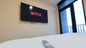 A bed with a remote control, a wall-mounted TV displaying 'NETFLIX,' and a window with a view.