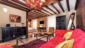 Una habitación con un sofá rojo, una araña, una televisión y una cama.