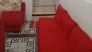 A staircase leading to an upper floor, a red sofa, a floral cushion, and a patterned floor.