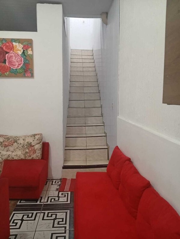 A staircase leading to an upper floor, a red sofa, a floral cushion, and a patterned floor.
