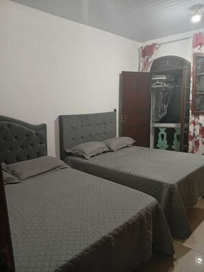 A room with two beds, a wardrobe, and a door leading to another room.