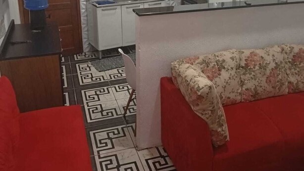 A compact kitchen with a refrigerator, sink, and window. There is a red sofa and a patterned rug.