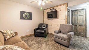 Ein Wohnzimmer mit Deckenventilator, zwei Sesseln, einer Couch, einem Kamin und einer Holztür.