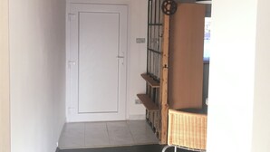 A hallway with a white door, wooden beams, a metal ladder, and a wicker basket. - 5 minutes to the center, 5 minutes to the forest, a cozy little apartment (Selb)