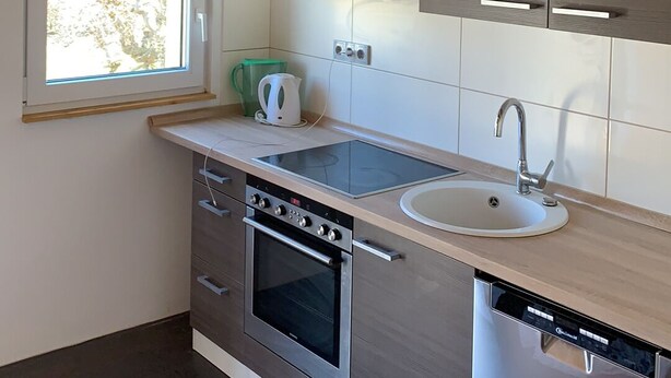 A modern kitchen with wooden beams, a large pendant light, a built-in oven, a dishwasher, and a window with a view. - 5 minutes to the center, 5 minutes to the forest, a cozy little apartment (Selb)