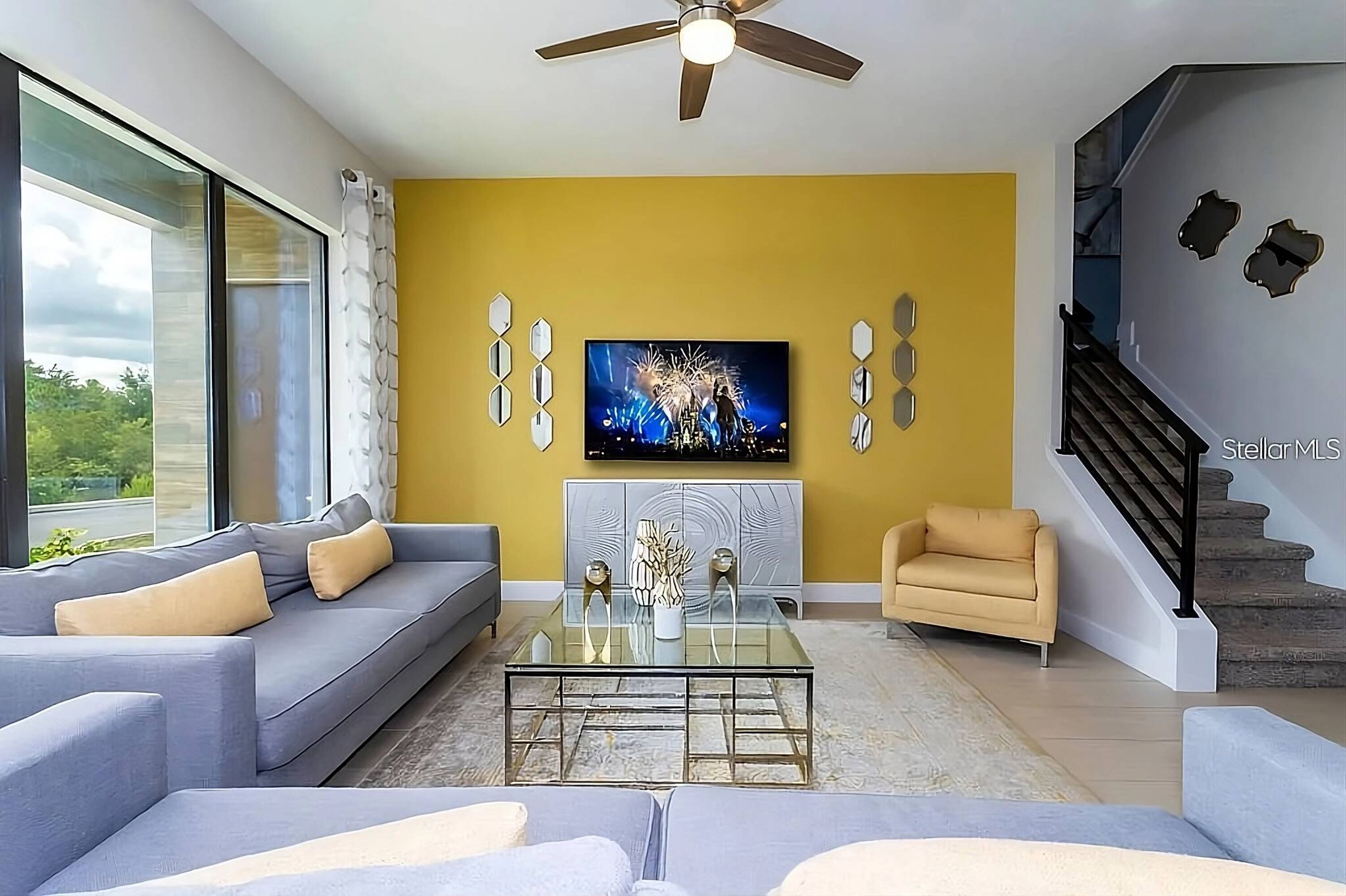 A modern living room with a sofa, a coffee table, a TV, and a staircase.