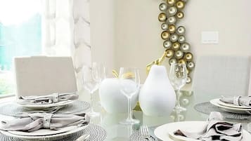 A dining table set with white plates, silverware, and clear glassware, surrounded by white vases and a gold decorative element.